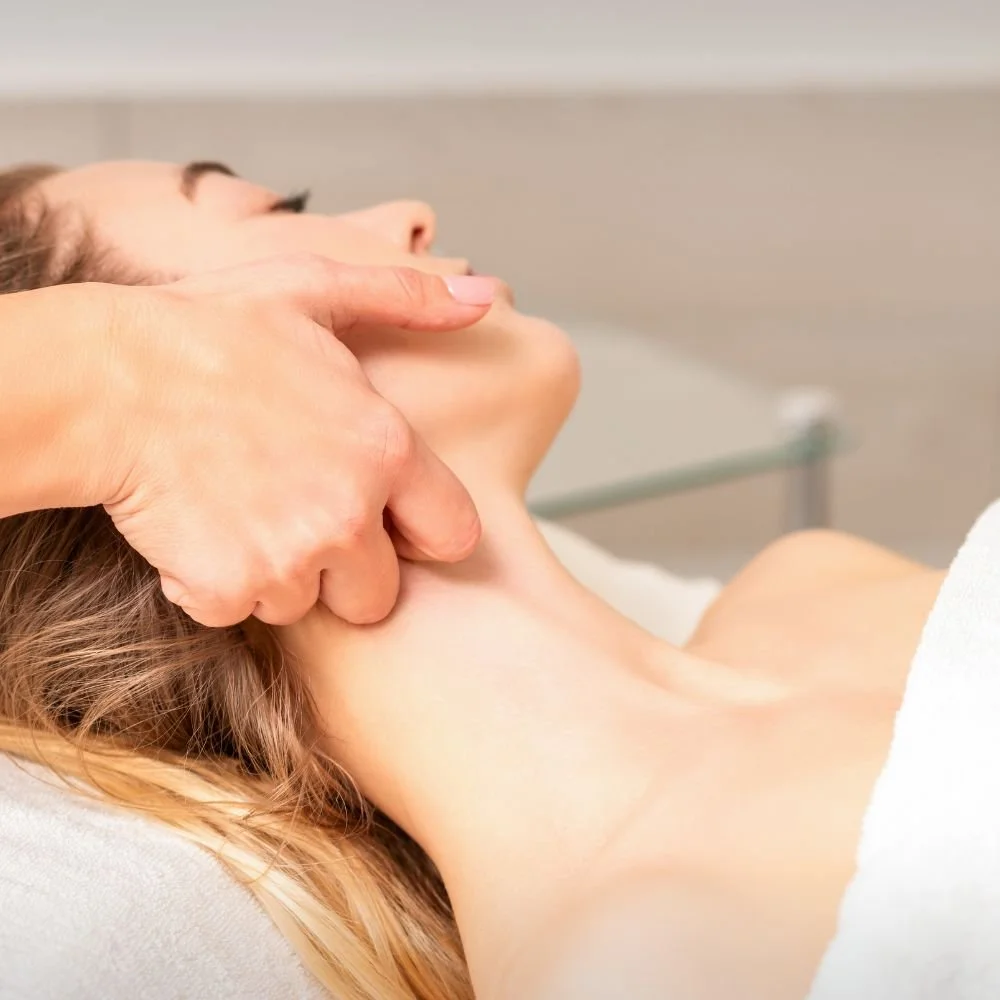 Person receiving a massage on their neck and throat area while lying down.