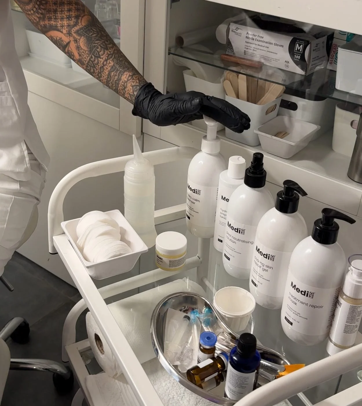 A medical workstation with various skincare and medical products, including bottles labeled 'Med' for med4, cotton pads, and medical gloves, in a clinical setting.