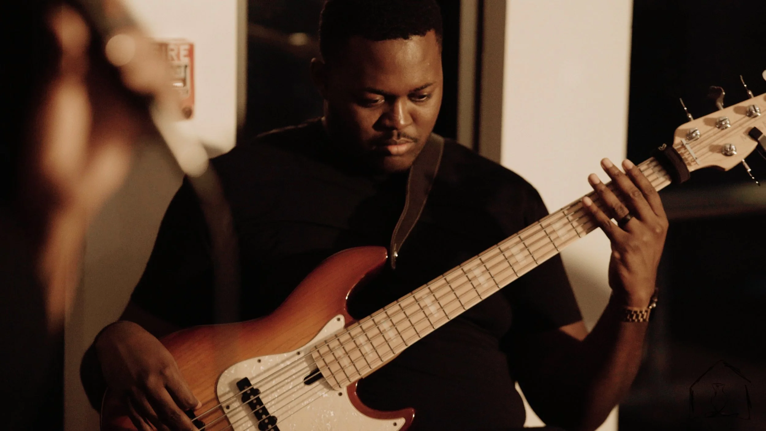 A man playing an electric bass guitar in a dimly lit room.