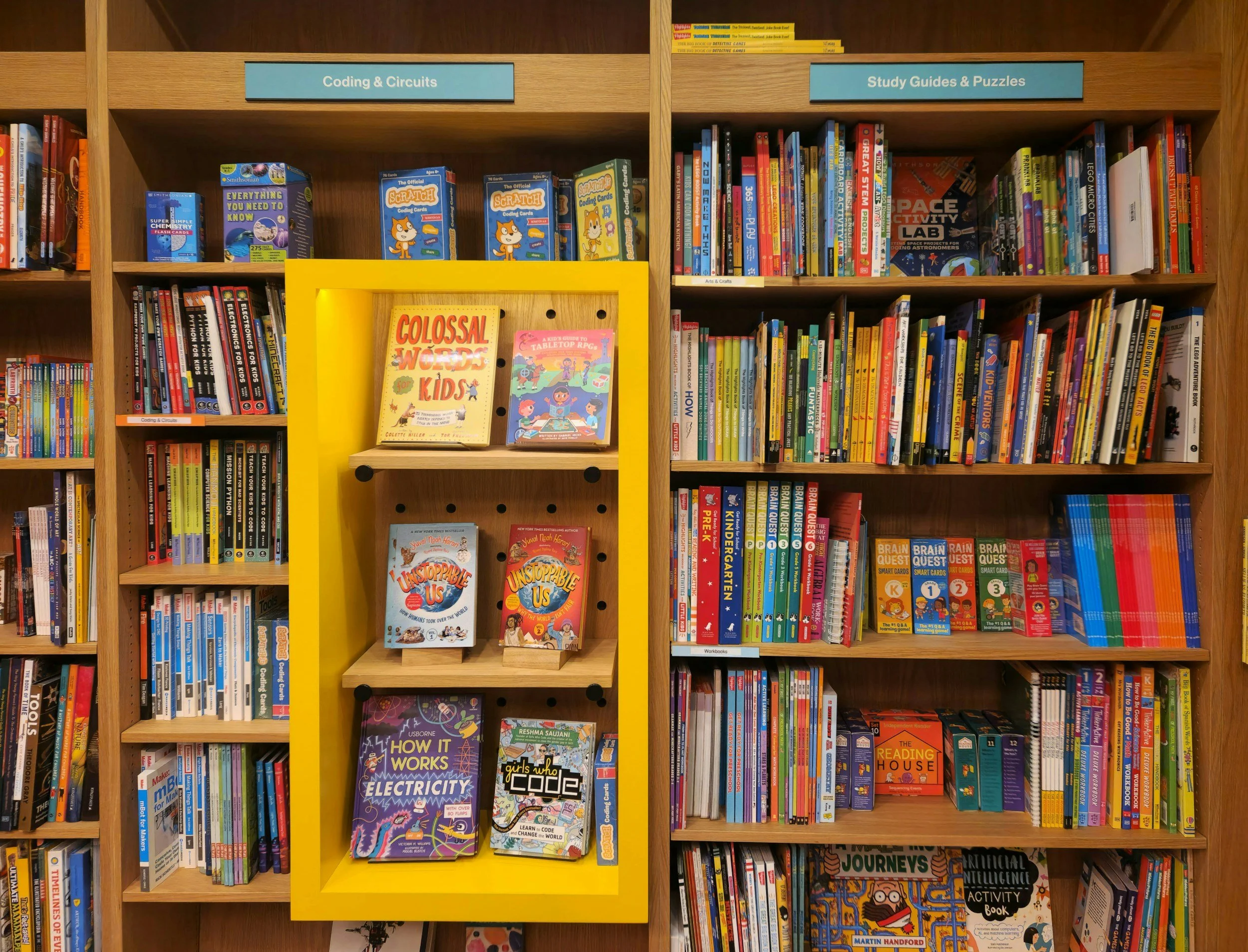 Bookshelves labeled 'Coding & Circuits' and 'Study Guides & Puzzles' with children's books and educational materials displayed, including titles about electricity, coding, and science.