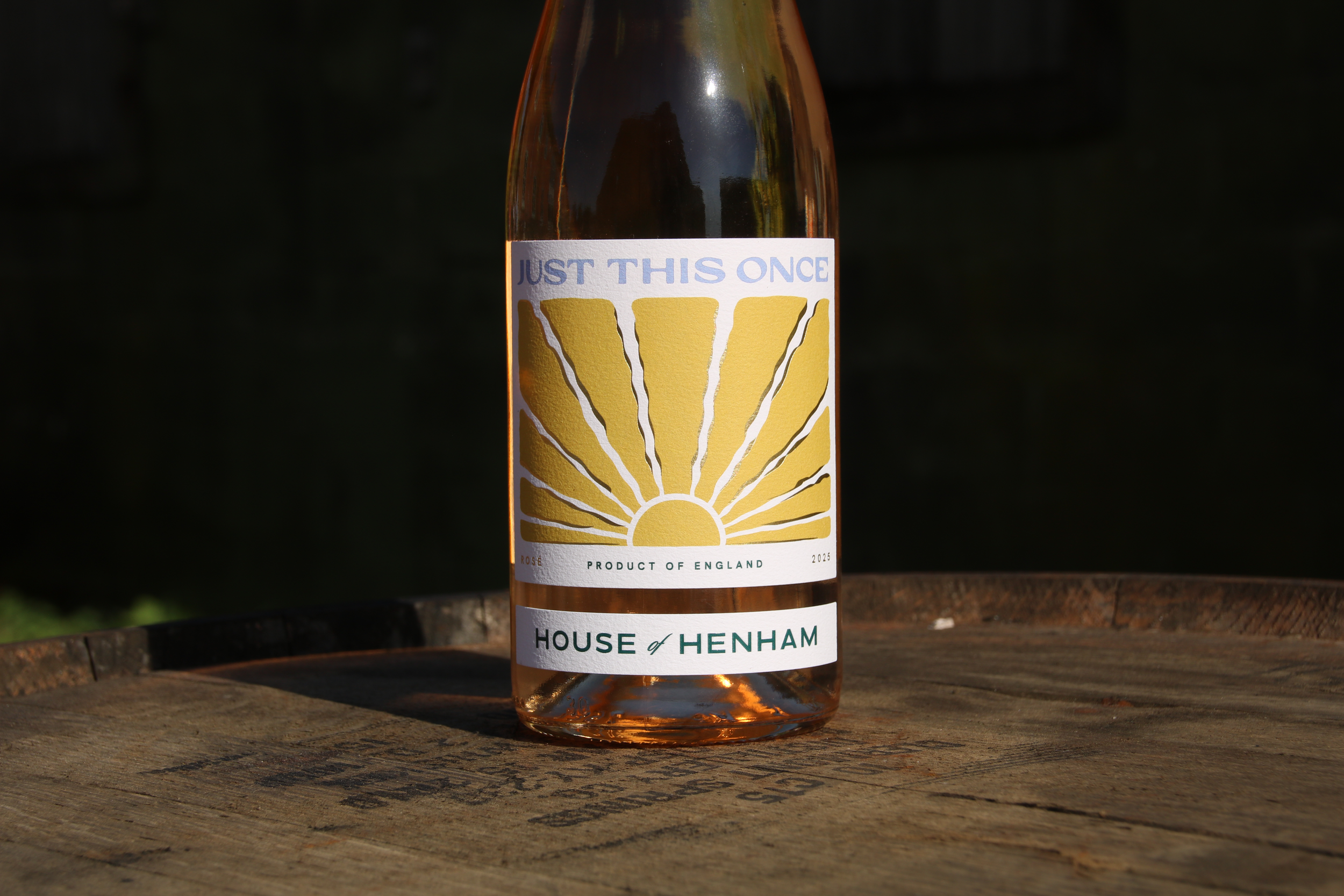 A bottle of premium Essex rosé wine with a white label that has a yellow design resembling a rising sun and the text 'Just This Once' and 'House of Henham'.