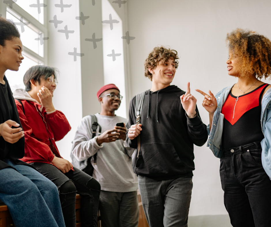 Group of diverse young people in a classroom or common area, engaging in conversation and smiling.