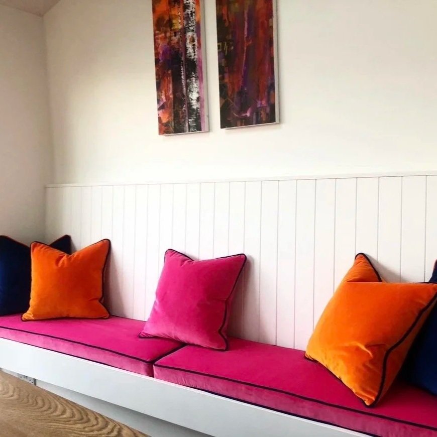 Colorful living room with a built-in white bench, pink cushions, and burnt orange and navy throw pillows, with abstract artwork hanging on the wall.