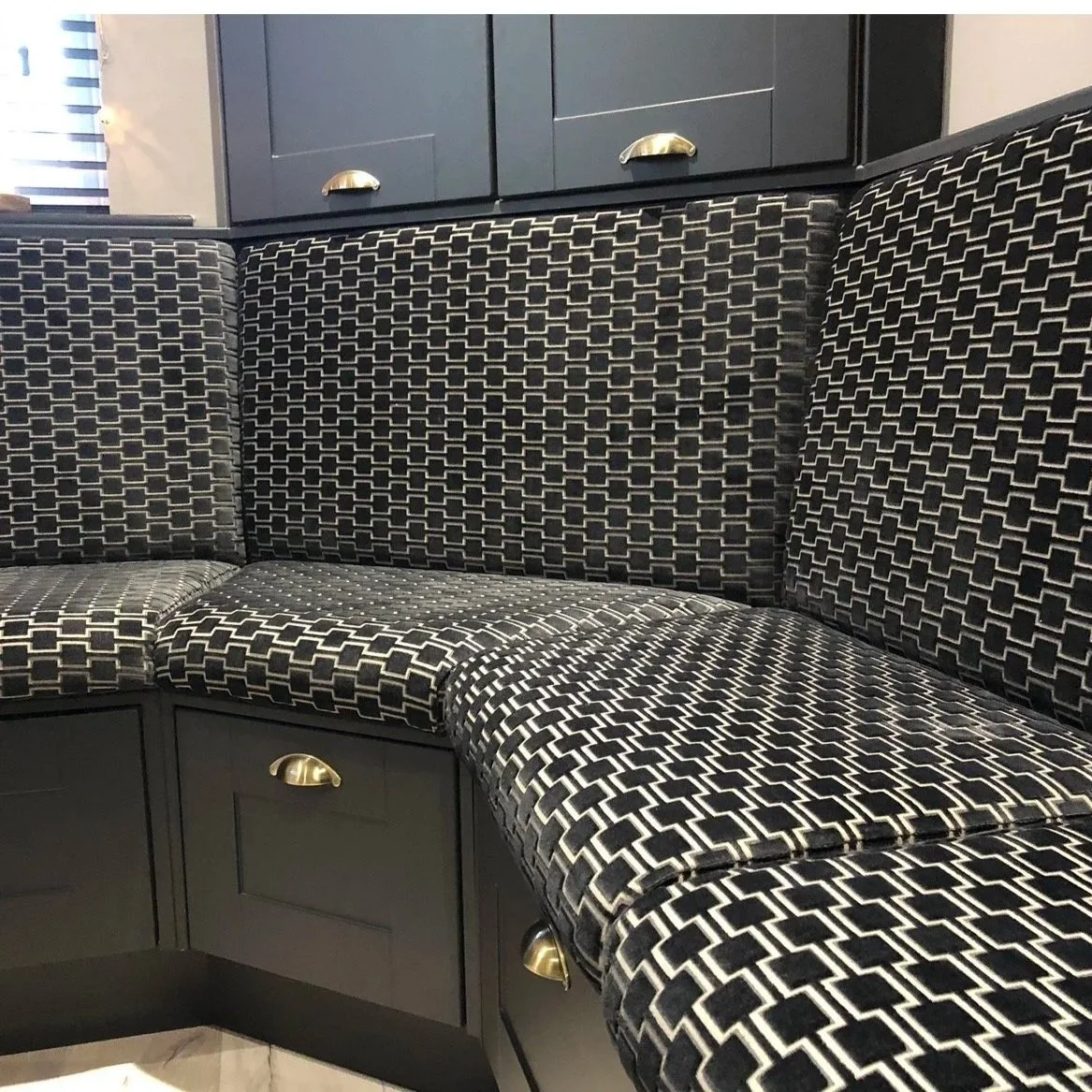 A black and white patterned upholstered corner bench with storage cabinets below, in a kitchen or dining area.