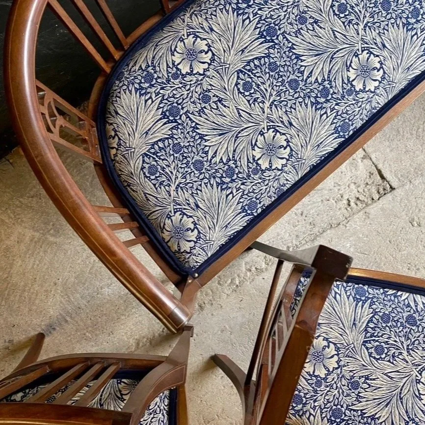 Three wooden chairs with blue and white floral-patterned cushions are arranged on a concrete floor.