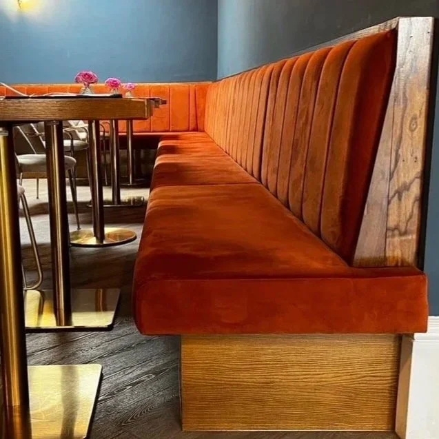 Long orange velvet booth seating along a wall in a restaurant with wooden accents.