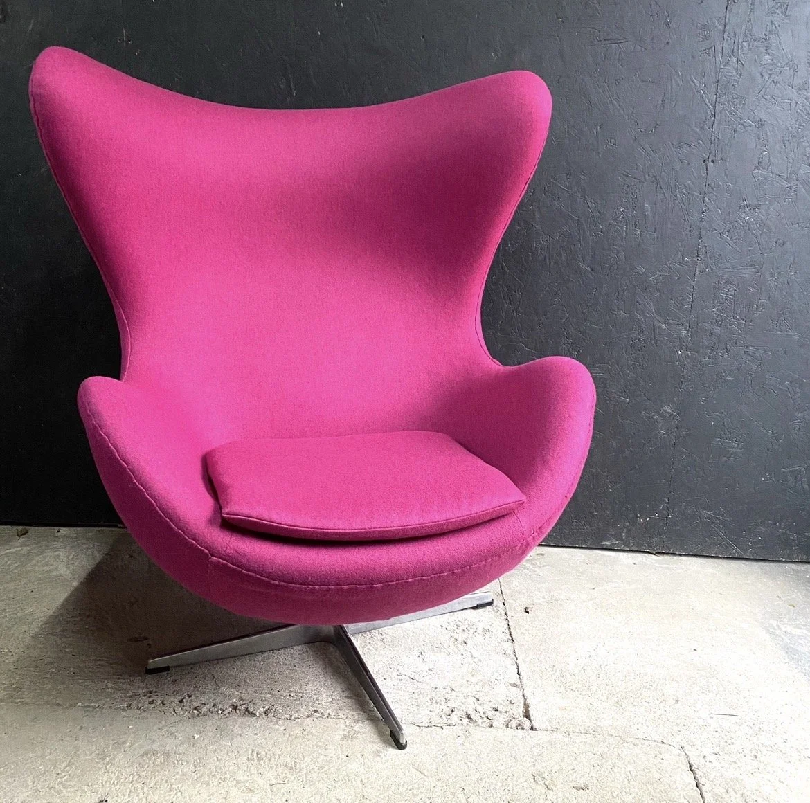 Pink modern armchair with a matching cushion against a dark wall.