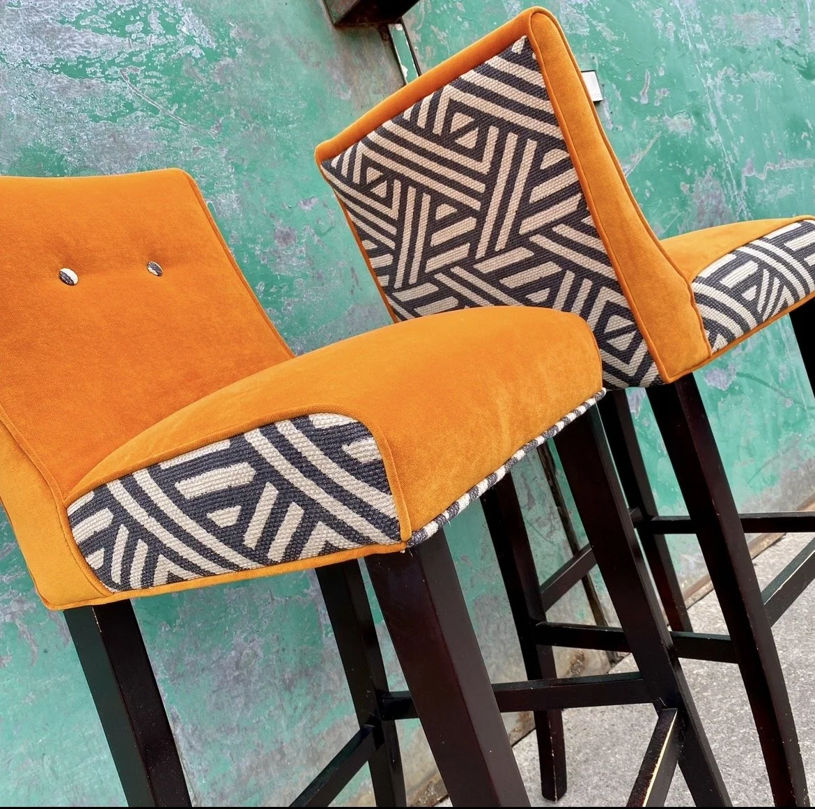 Orange bar stools with patterned cushions and black legs, set against a distressed green concrete floor.