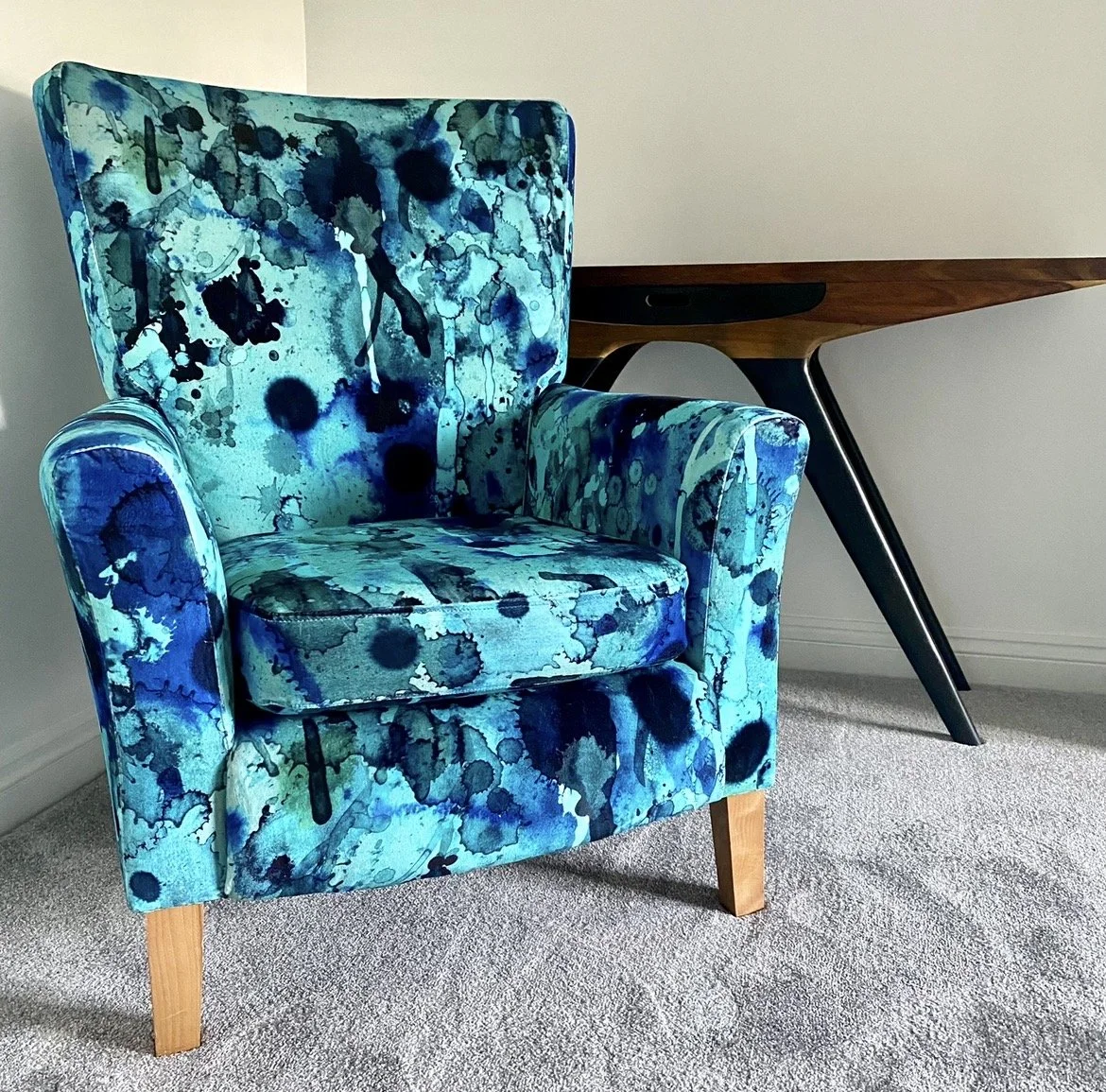 A blue patterned armchair next to a wooden table against a plain wall.