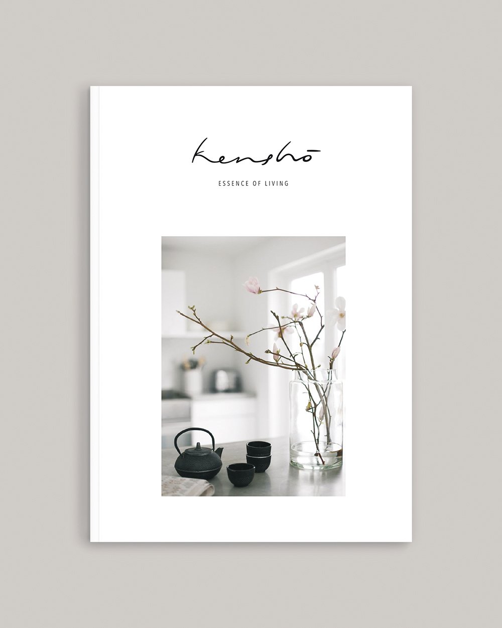 Buchcover mit der Aufschrift "Kensho" und dem Untertitel "Essence of Living". Das Bild zeigt eine Vase mit Zweigen und Blüten sowie schwarze Teekannen und -tassen auf einem Tisch.