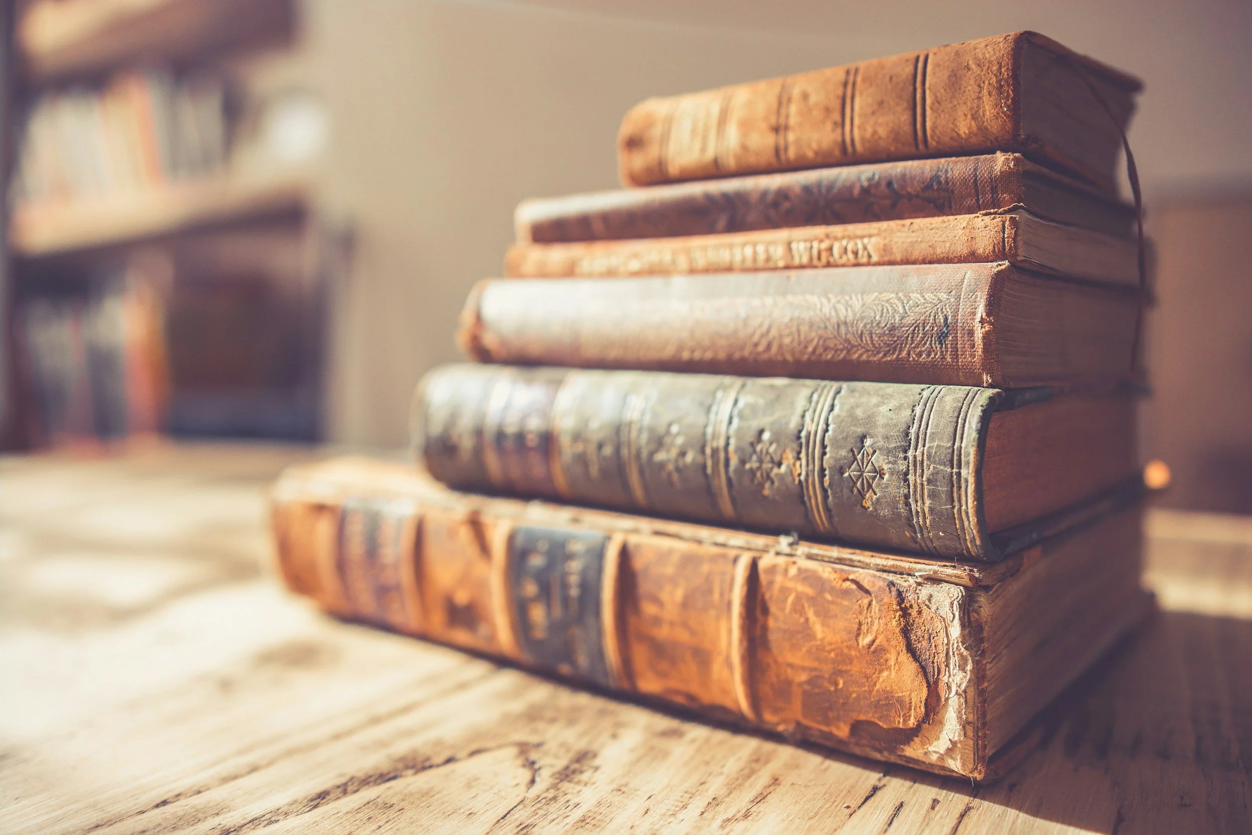 A stack of old, leather-bound books on a wooden surface with a blurred background.
