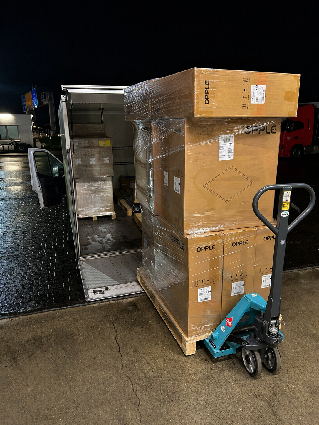 Ladung mit Kartons auf Paletten, einige sind noch auf einer Rollkarre, auf einem LKW bei Nacht