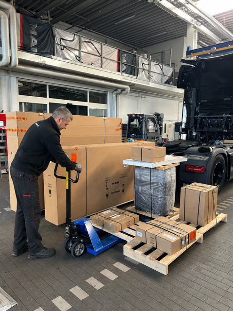 Mitarbeiter in einer Lagerhalle nutzt einen elektrischen Palettenroller, um große Kisten zu bewegen.