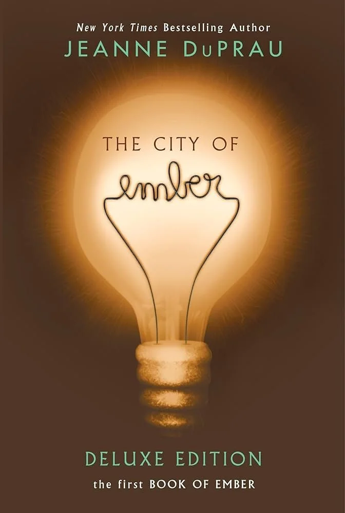 Book cover for 'The City of Ember' by Jeanne DuPrau, featuring a glowing light bulb with the word 'ember' written inside in cursive, and the subtitle 'Deluxe Edition' at the bottom.