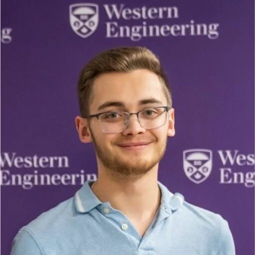 Young man with glasses and a light blue polo shirt standing in front of a purple backdrop with Western Engineering logo and text.