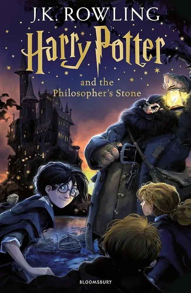 Book cover of "Harry Potter and the Philosopher's Stone" by J.K. Rowling, featuring Harry Potter with glasses, Ron and Hermione, and Hagrid holding a lantern, with a castle in the background.