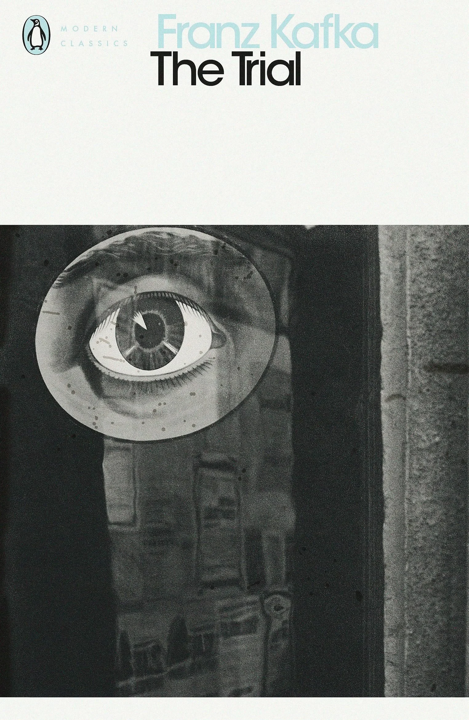 The image features the book cover of 'The Trial' by Franz Kafka, part of the Modern Classics series, with a black and white illustration of an eye on a dark background.