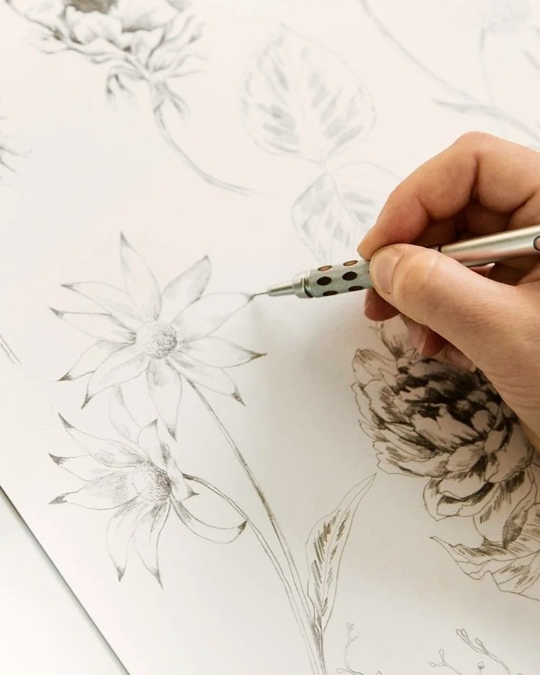 A person sketching flowers on paper with a pen.