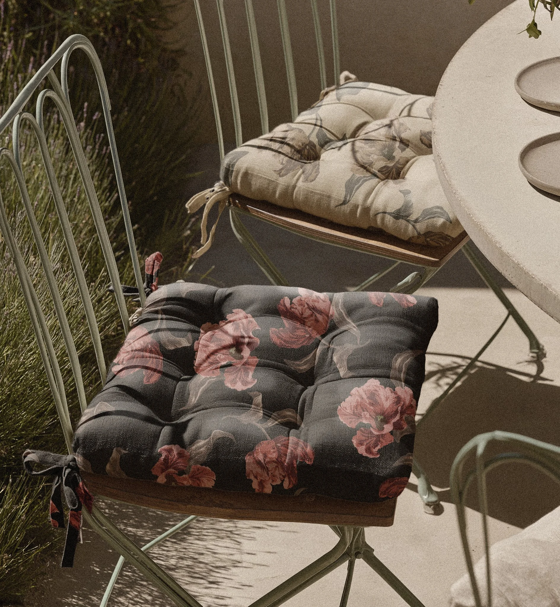 View of a metal garden chair with a cushioned seat, a table with matching dishes, and greenery in the background, taken indoors.