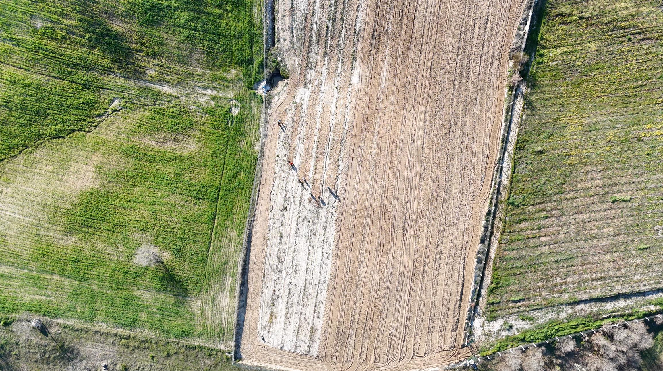Aerial view of a construction site with cleared land and workers, surrounded by green fields and suggestive of farmland or vineyards.