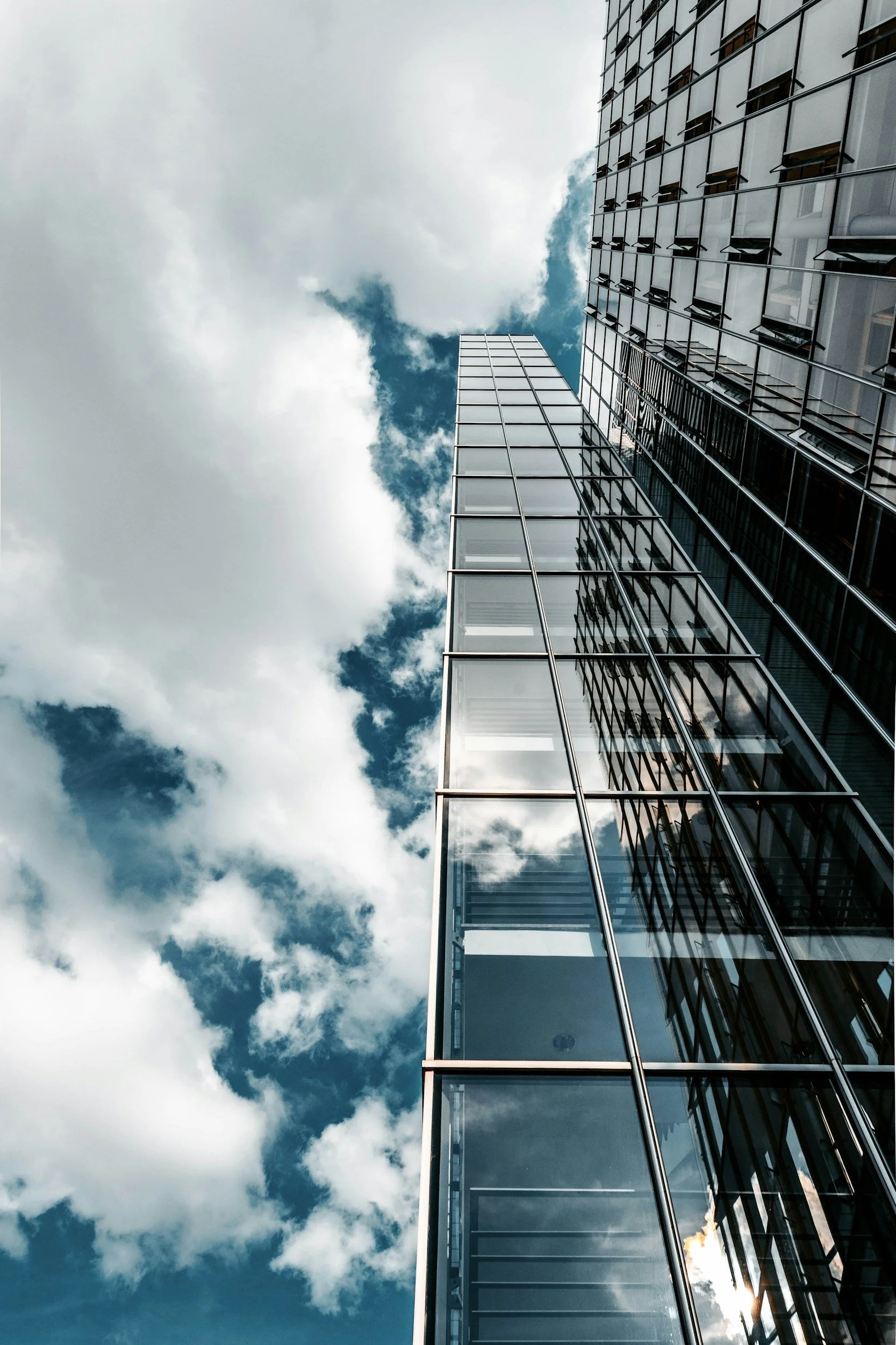 Vue d'une façade de gratte-ciel en verre sous un ciel avec des nuages, prise en contre-plongée.