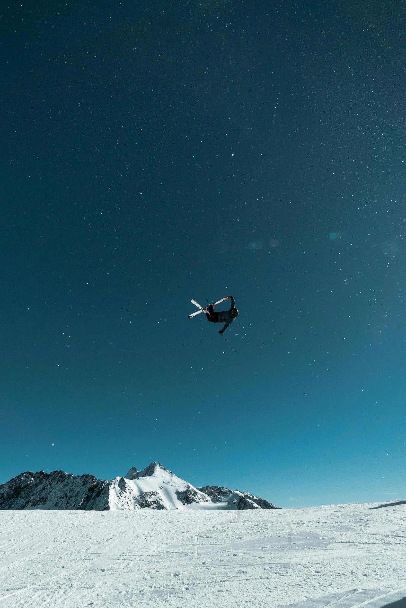 Un skieur dévalant une pente enneigée en montagne sous un ciel étoilé.