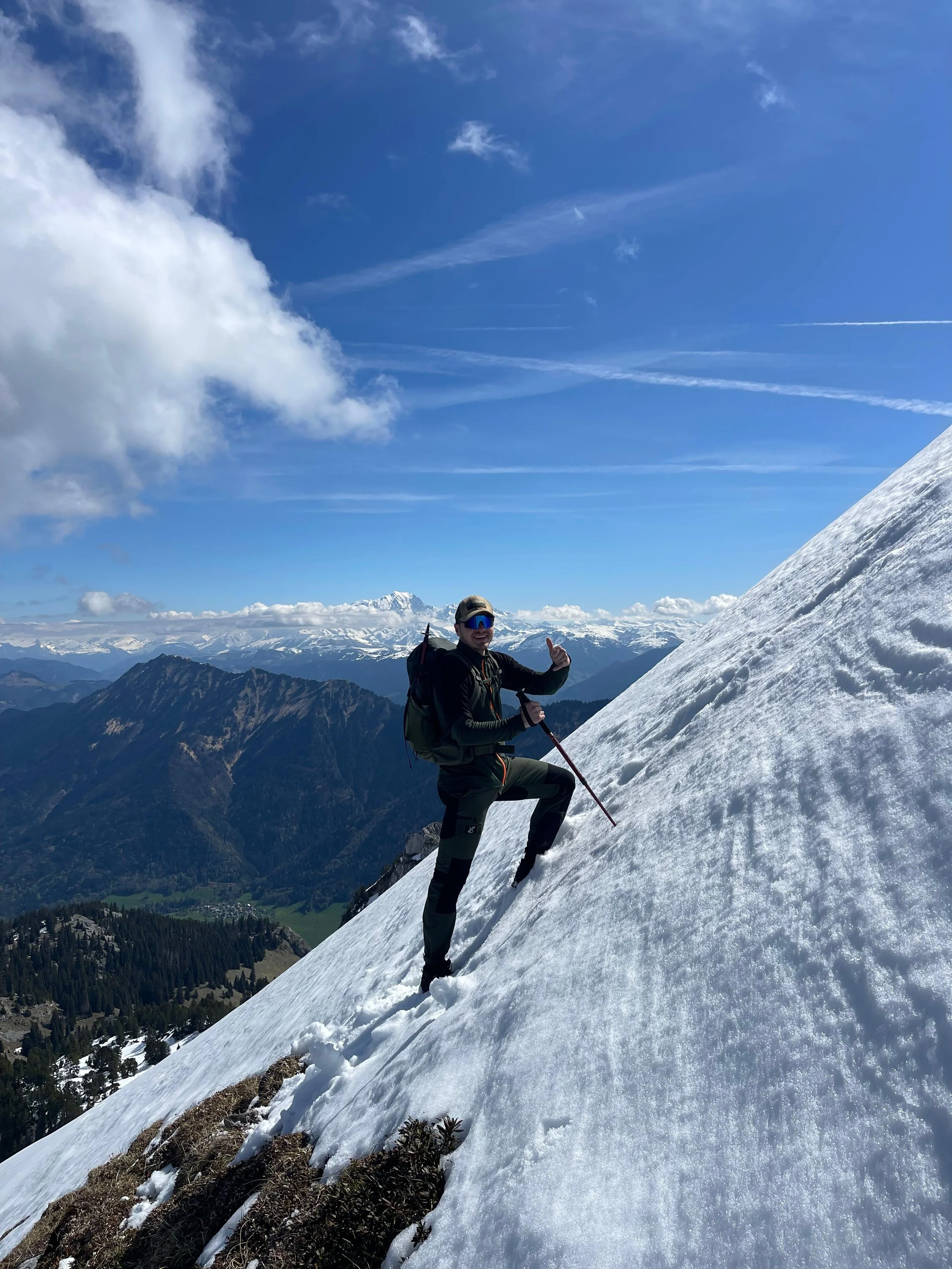 Homme en vêtements de ski sur une montagne enneigée avec un paysage de montagnes et un ciel bleu avec quelques nuages.