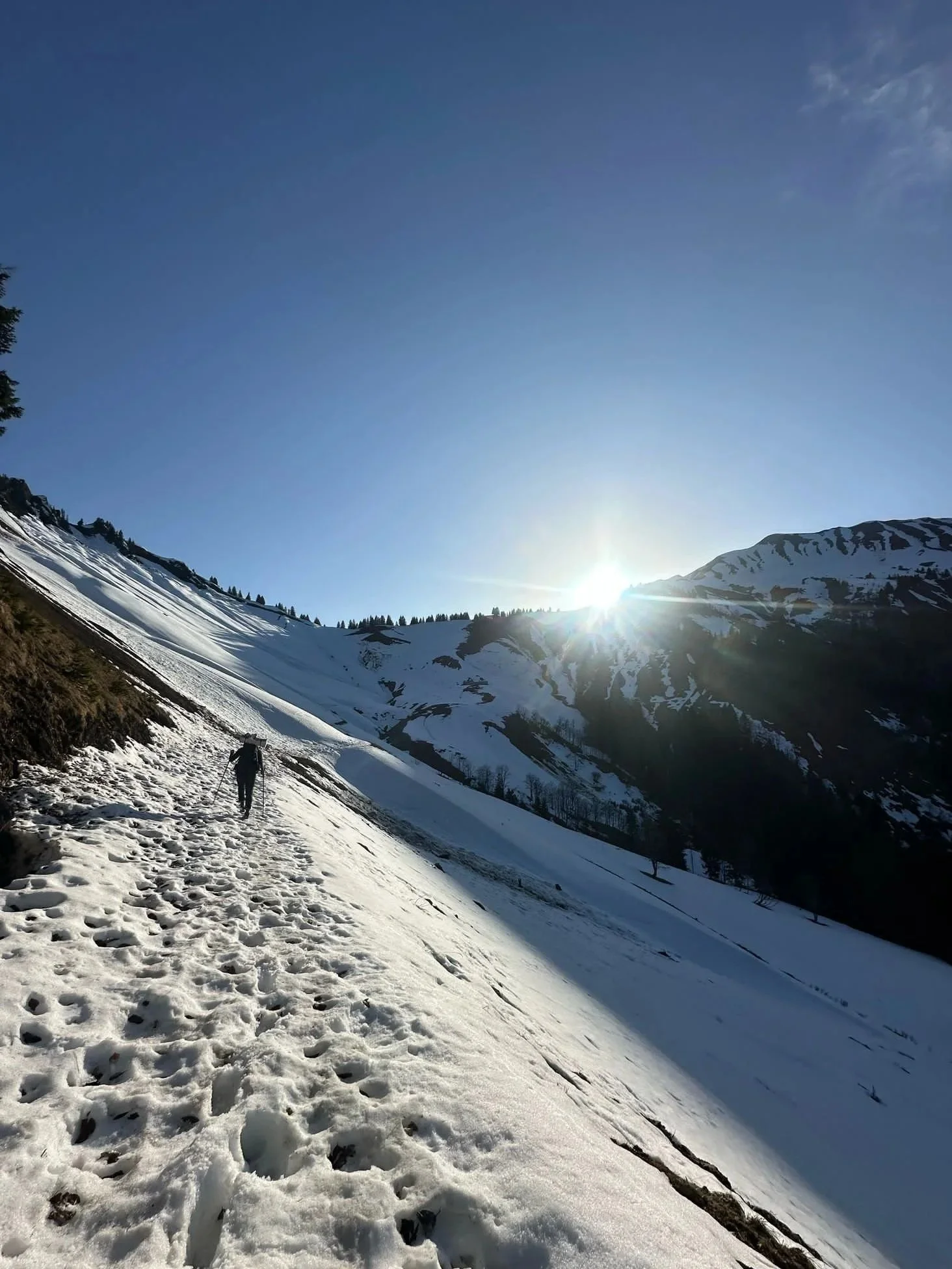 Paysage de montagnes enneigées au soleil avec un ciel clair et une personne marchant dans la neige.
