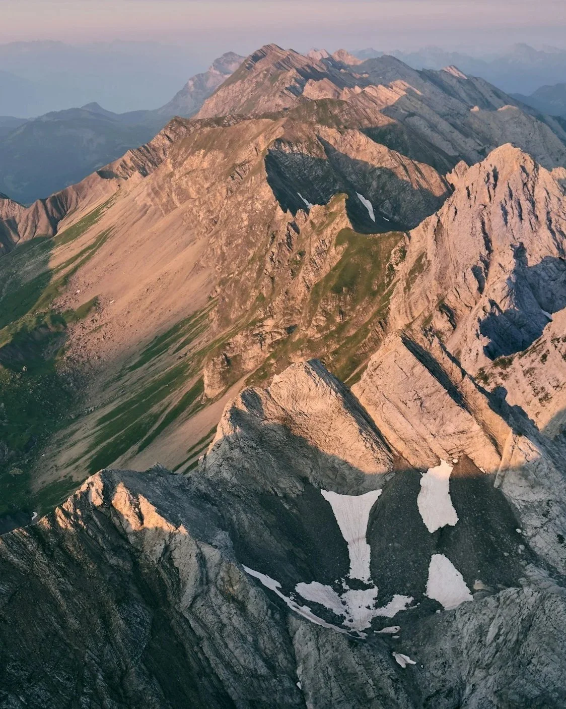 Montagnes rocheuses avec quelques restes de neige et des rochers impressionnants, probablement au lever ou coucher du soleil.