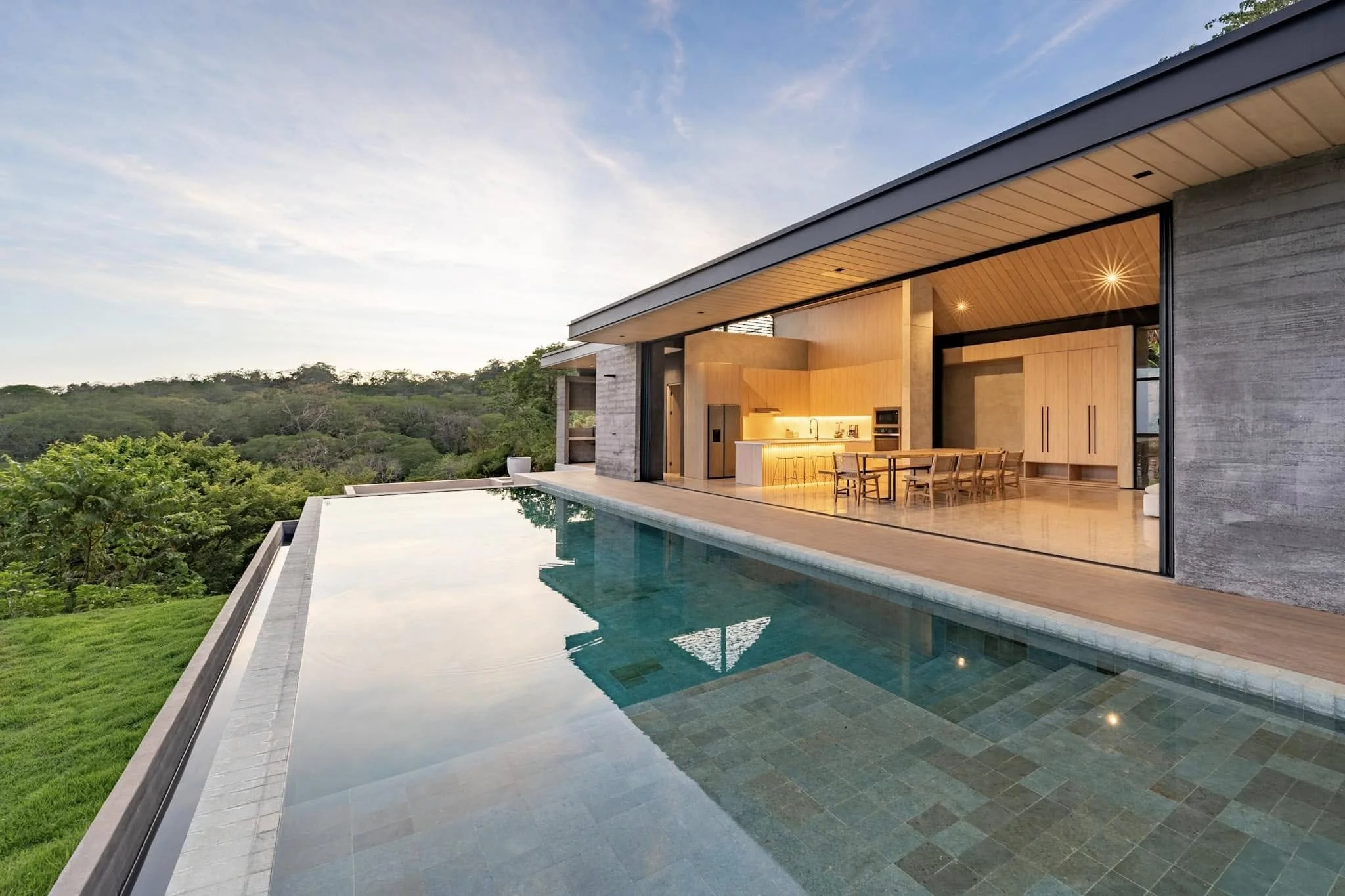 Modern house with outdoor pool and scenic view of forest at sunset