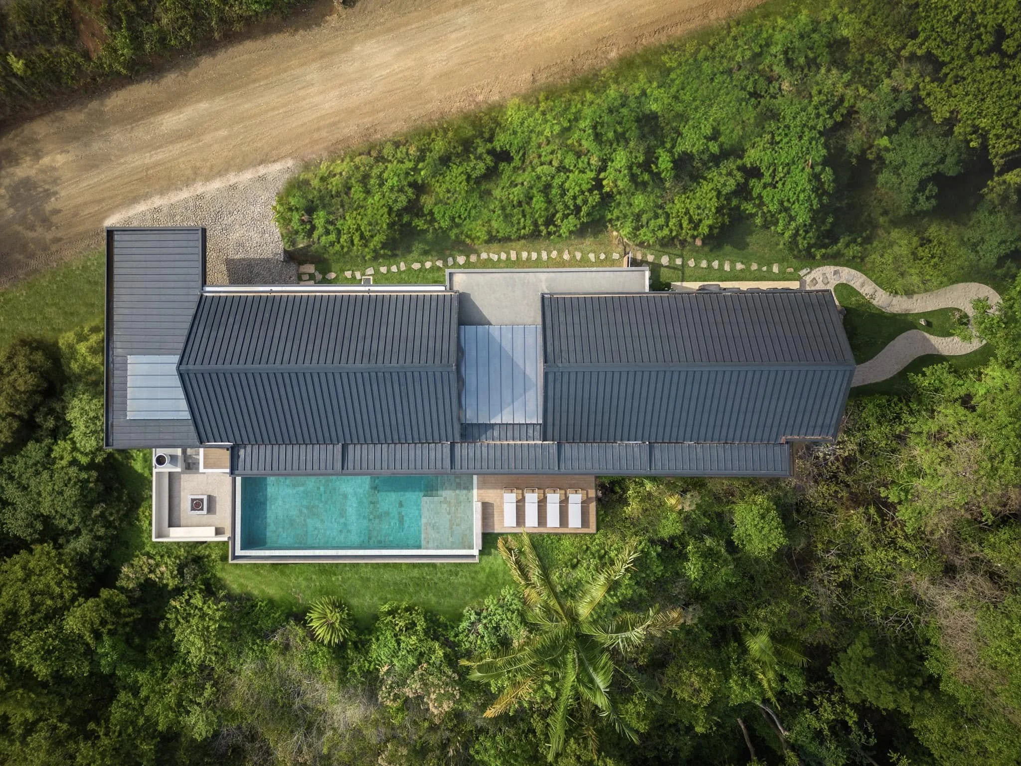 Aerial view of a modern house with a swimming pool surrounded by lush green trees and a lawn.