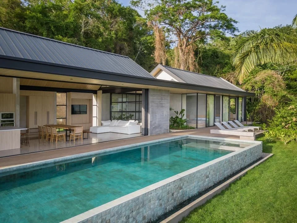Modern house with large swimming pool, outdoor lounge area, and tropical greenery.