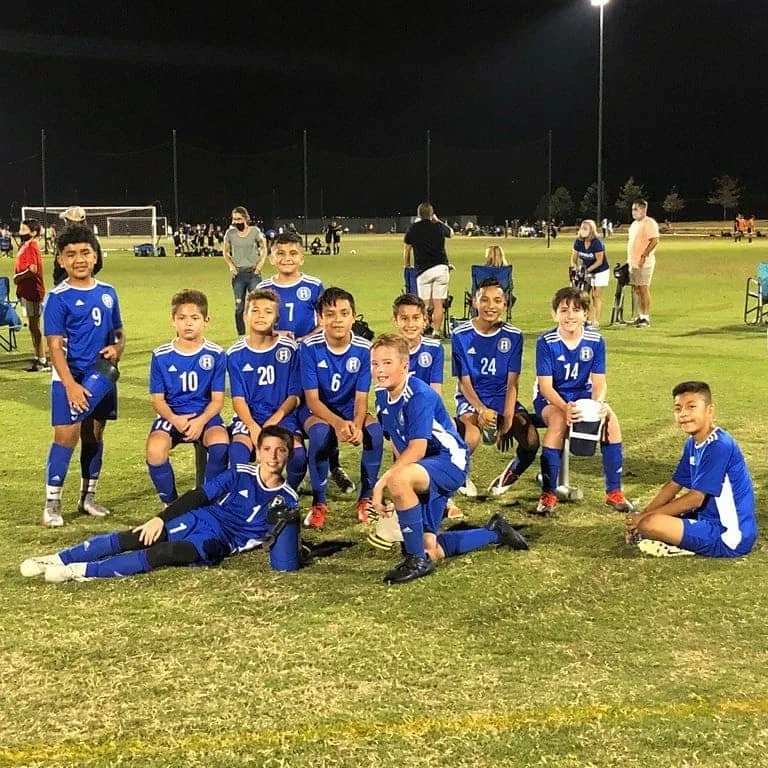 Young soccer players in blue Waco Soccer Club uniforms posing for a picture on a soccer field at night.