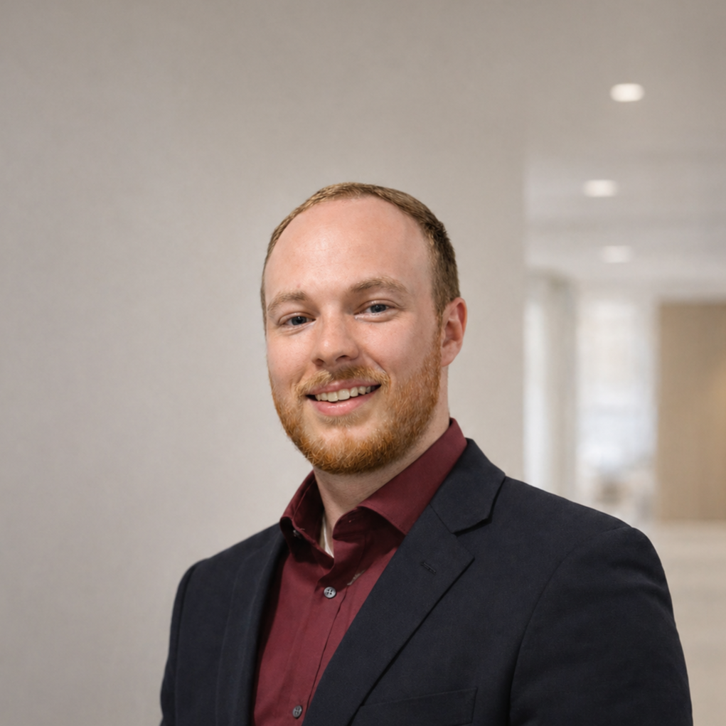 A man with red hair and beard wearing a dark blazer and maroon shirt, smiling in a professional setting. Founder of Waco SC