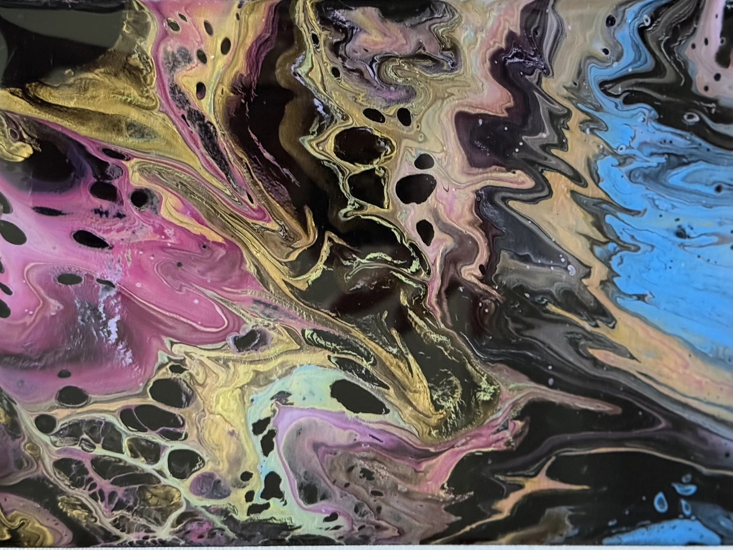 Abstract acrylic pour painting with swirling colors including black, yellow, pink, blue, purple, and gold, creating a marbled effect with organic patterns.