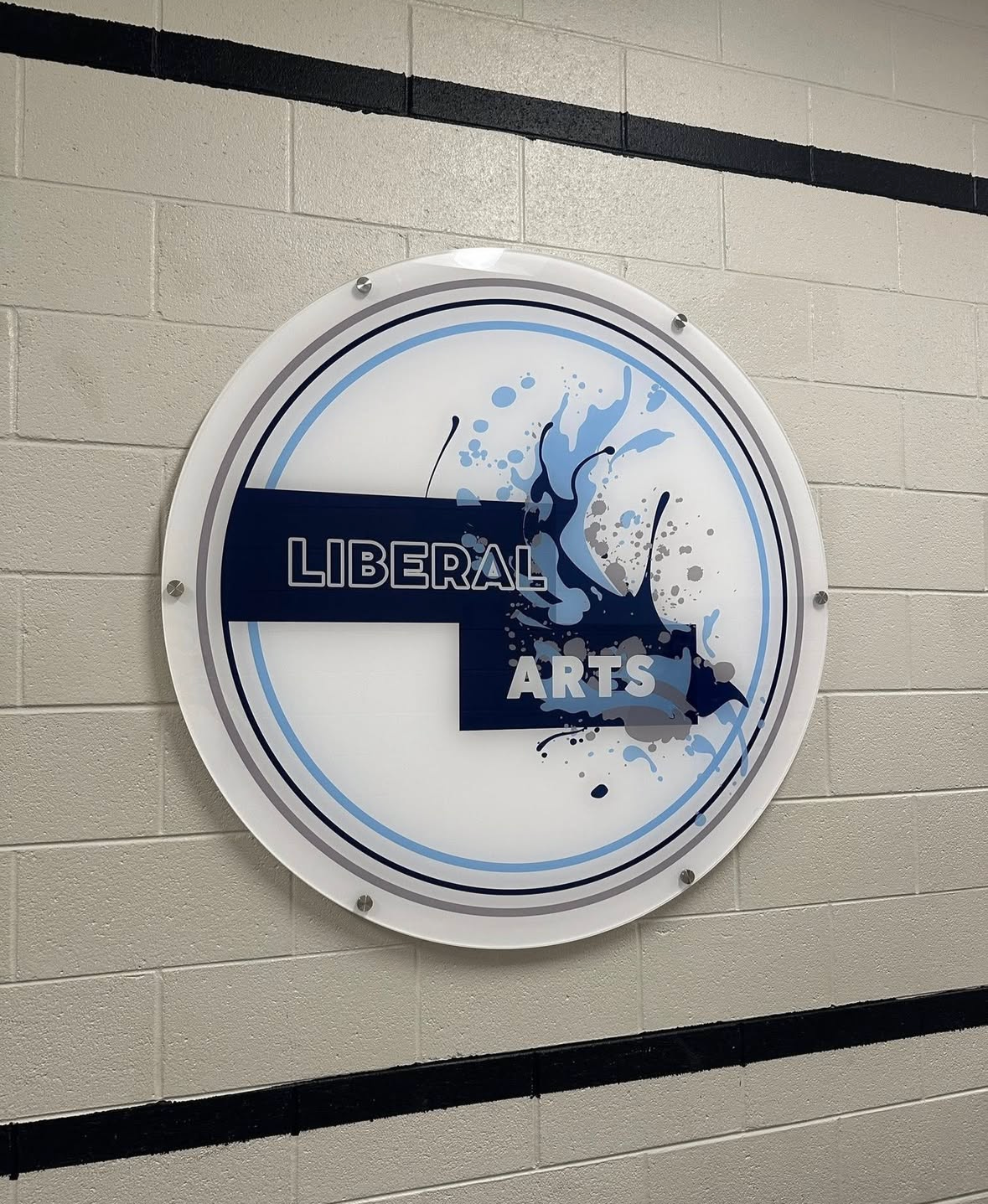 A circular sign on a beige brick wall that says 'Liberal Arts' with blue and gray splash design elements.