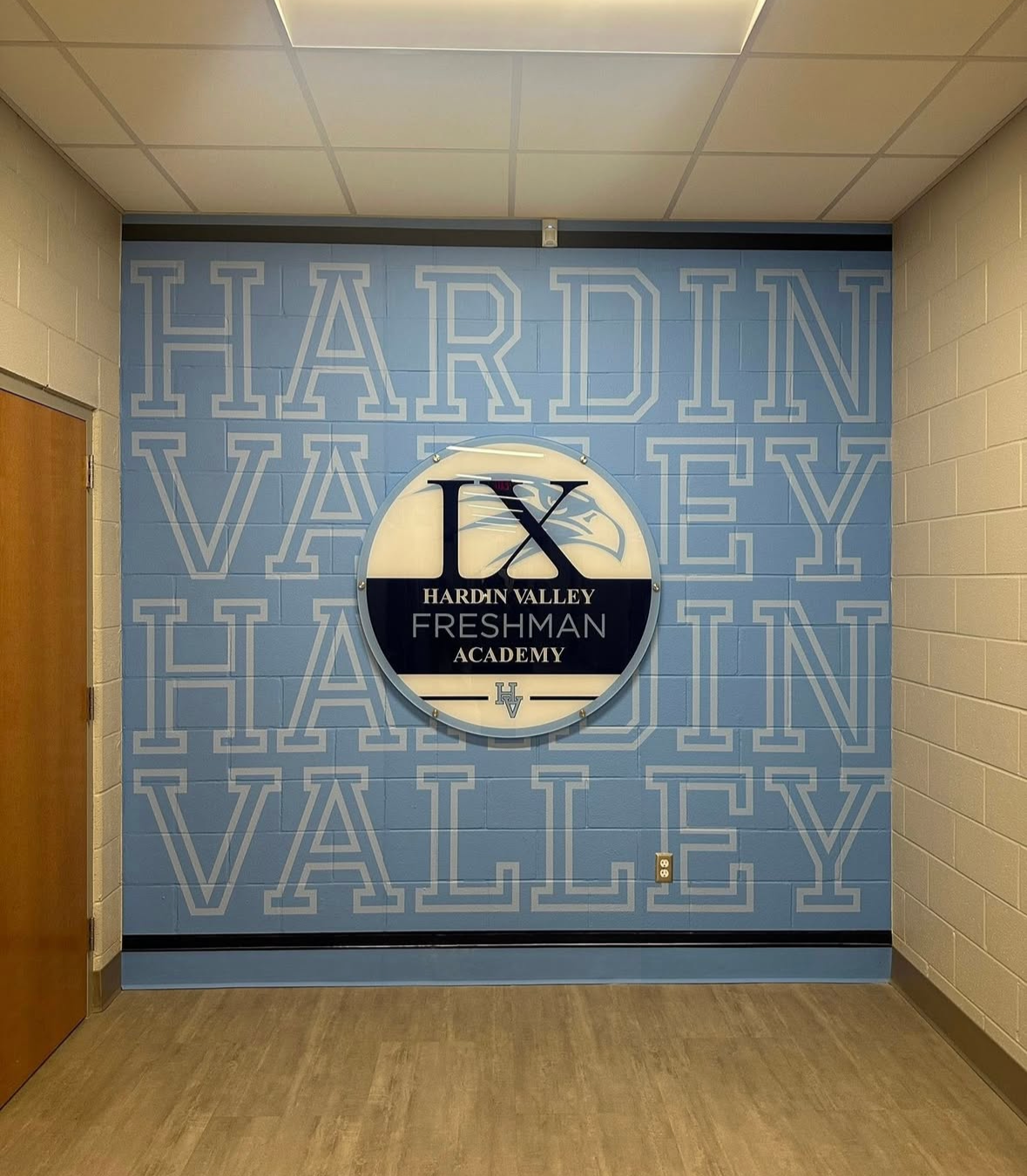 Wall with a large logo for Hardin Valley Freshman Academy, featuring a circular sign with the school initials and name, and a background pattern spelling out 'HARDIN VALLEY'.