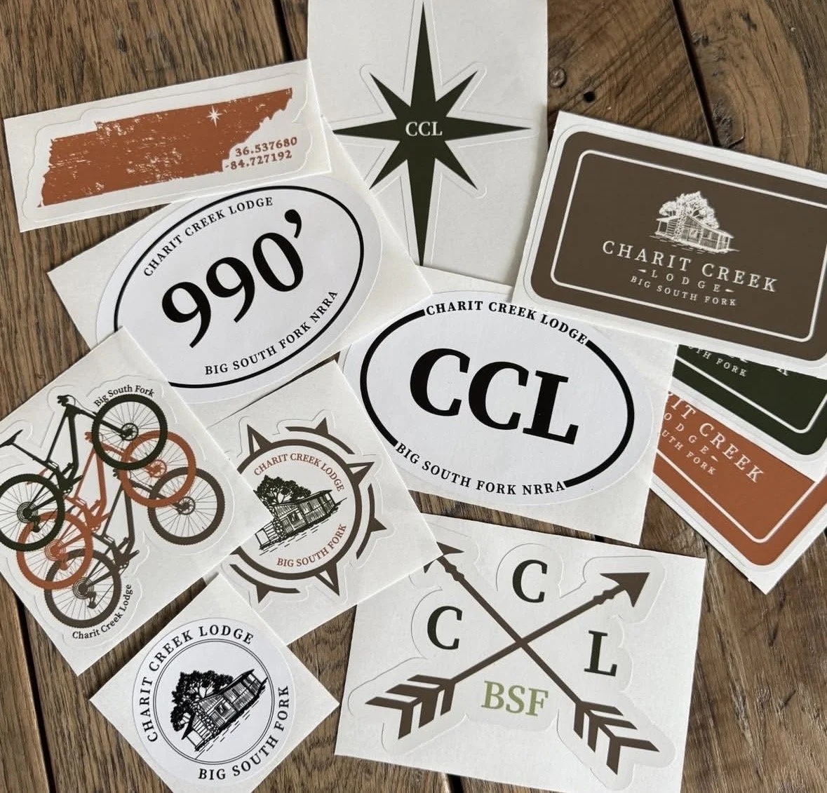 Collection of stickers and decals featuring logos, slogans, and graphics related to Charit Creek Lodge and Big South Fork NRRA, including a mountain silhouette, a compass, a bicycle, and crossed arrows with the letters C and L.