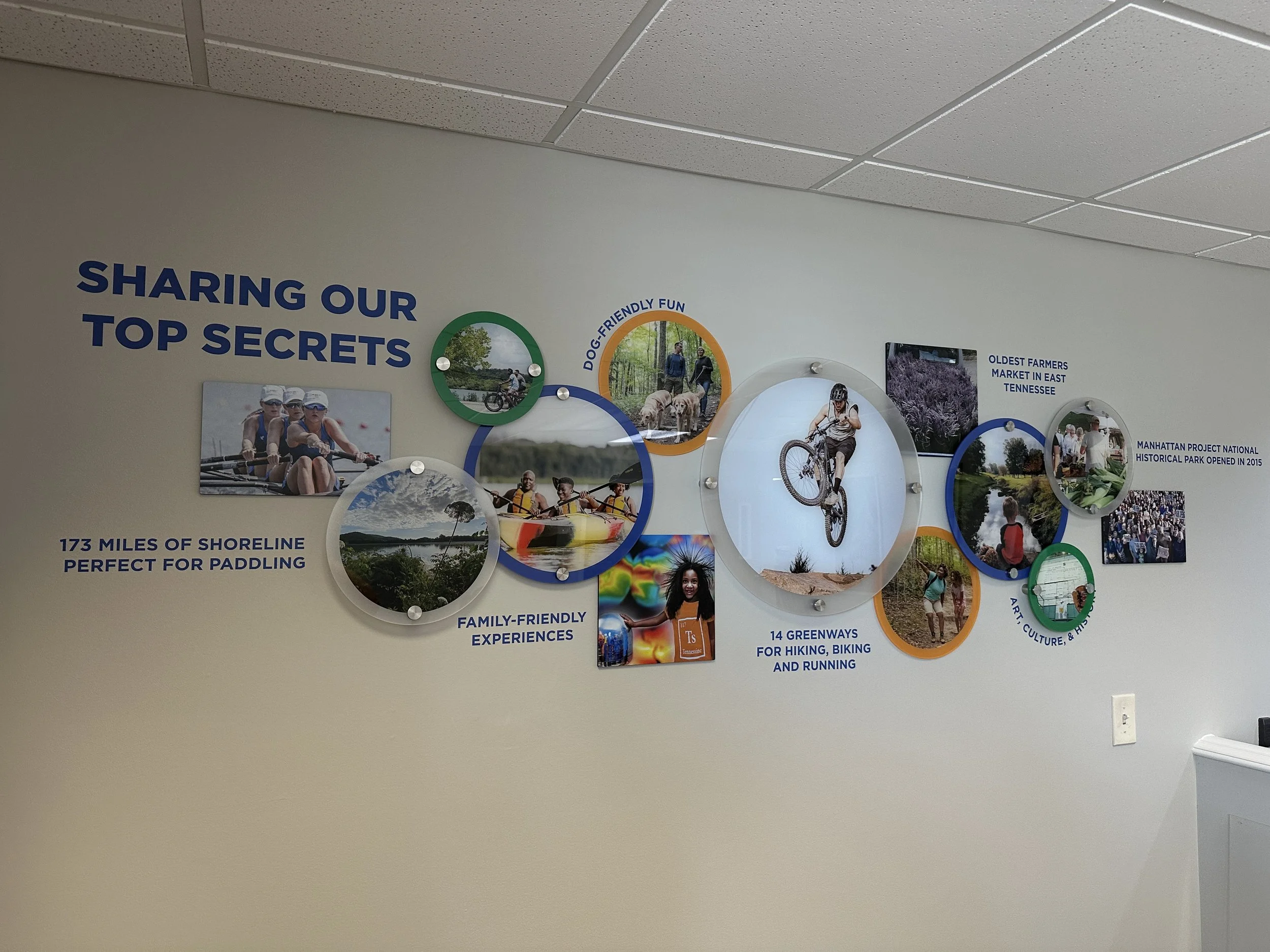 Wall display with the title 'Sharing Our Top Secrets' and various photos of outdoor activities, including biking, kayaking, and family experiences, highlighting Tennessee's natural and recreational attractions.