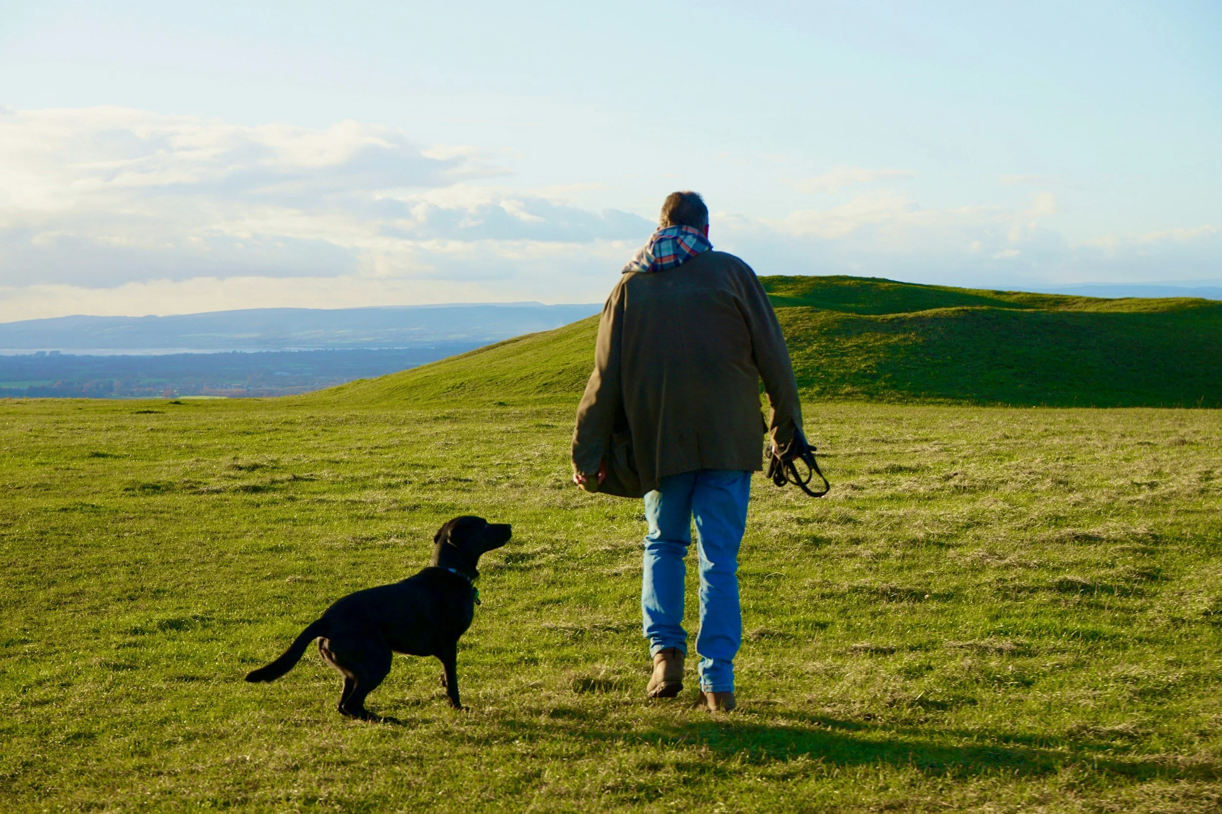 Dog owner walking a dog across open countryside - professional dog sitting by Skye & Paws