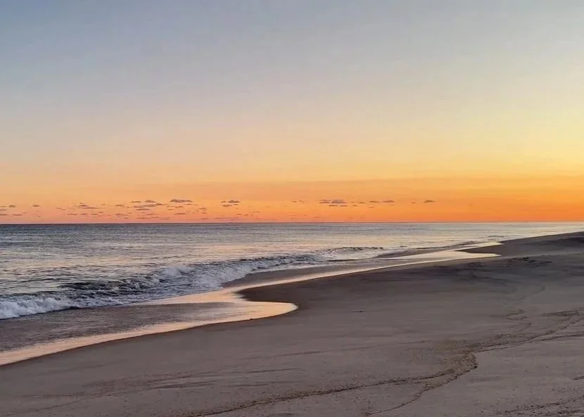 A peaceful beach scene at sunset with gentle waves and a colorful sky.