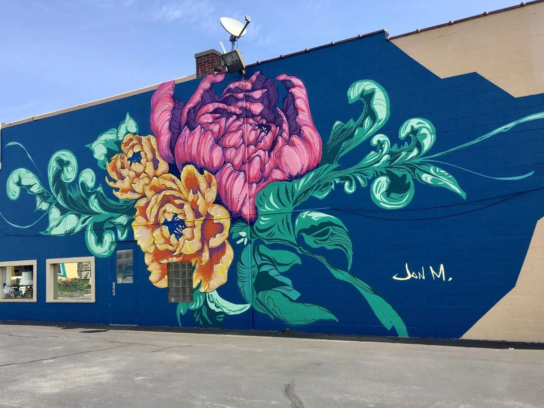 Peony blossoms and sweeping ornamental foliage, create a sense of motion across the architecture. The bold palette contrasts against deep blue, making the mural highly visible and engaging from distance. The piece was a community supported project ma