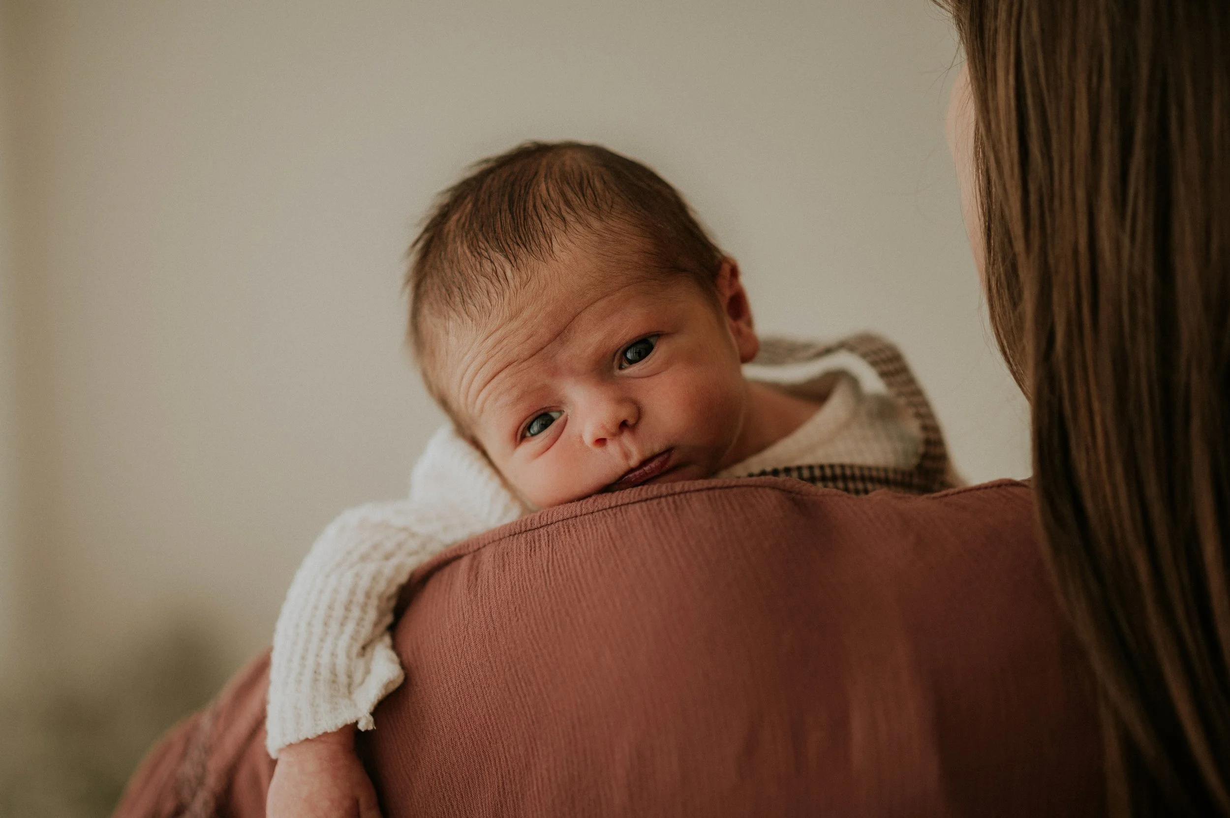 Close-up of a newborn baby resting on a woman's shoulder, with the woman partially visible and the baby's face in focus.
