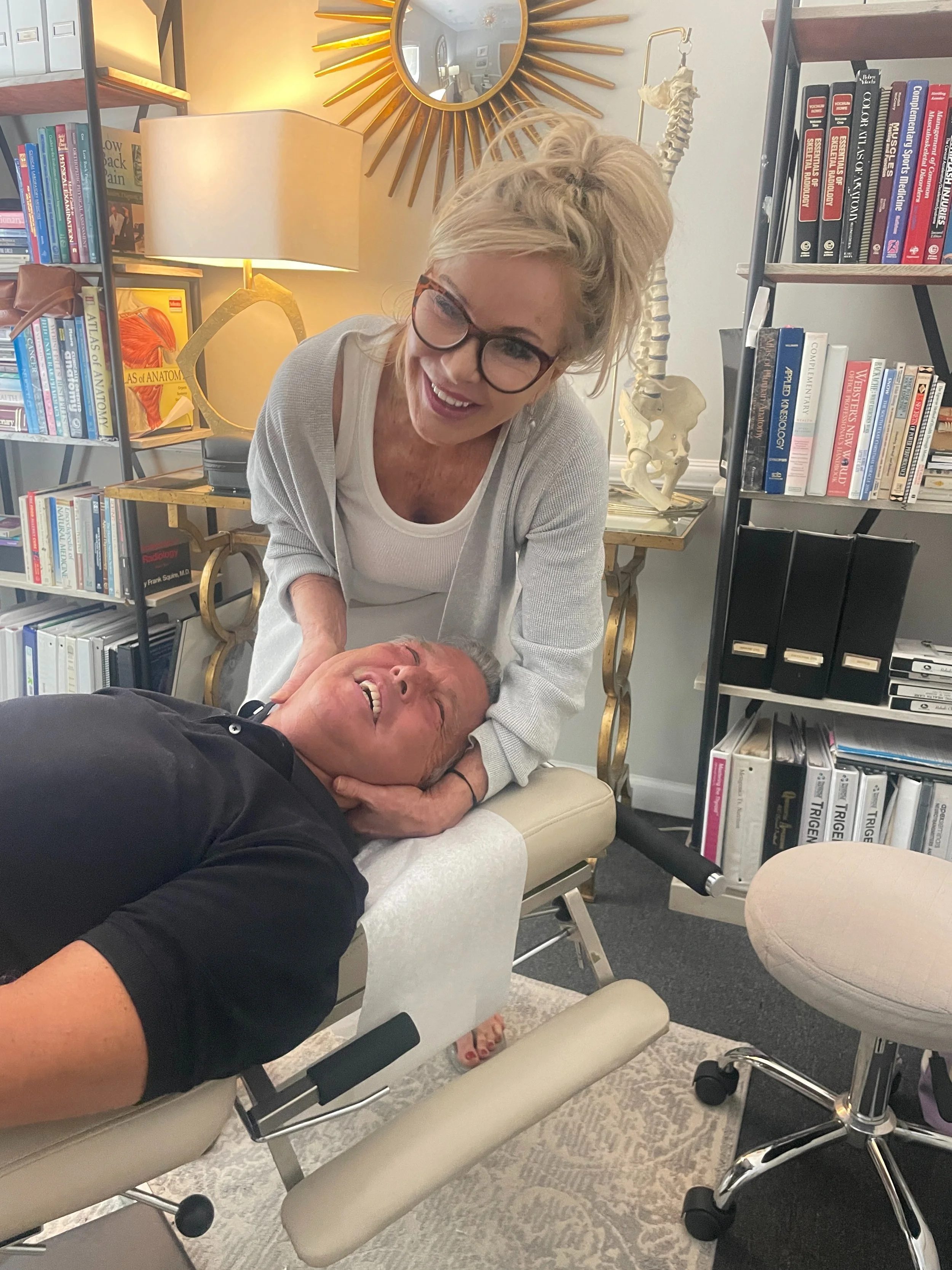 smiling chiropractor and smiling male patient while chiropractor does neck adjustment on table