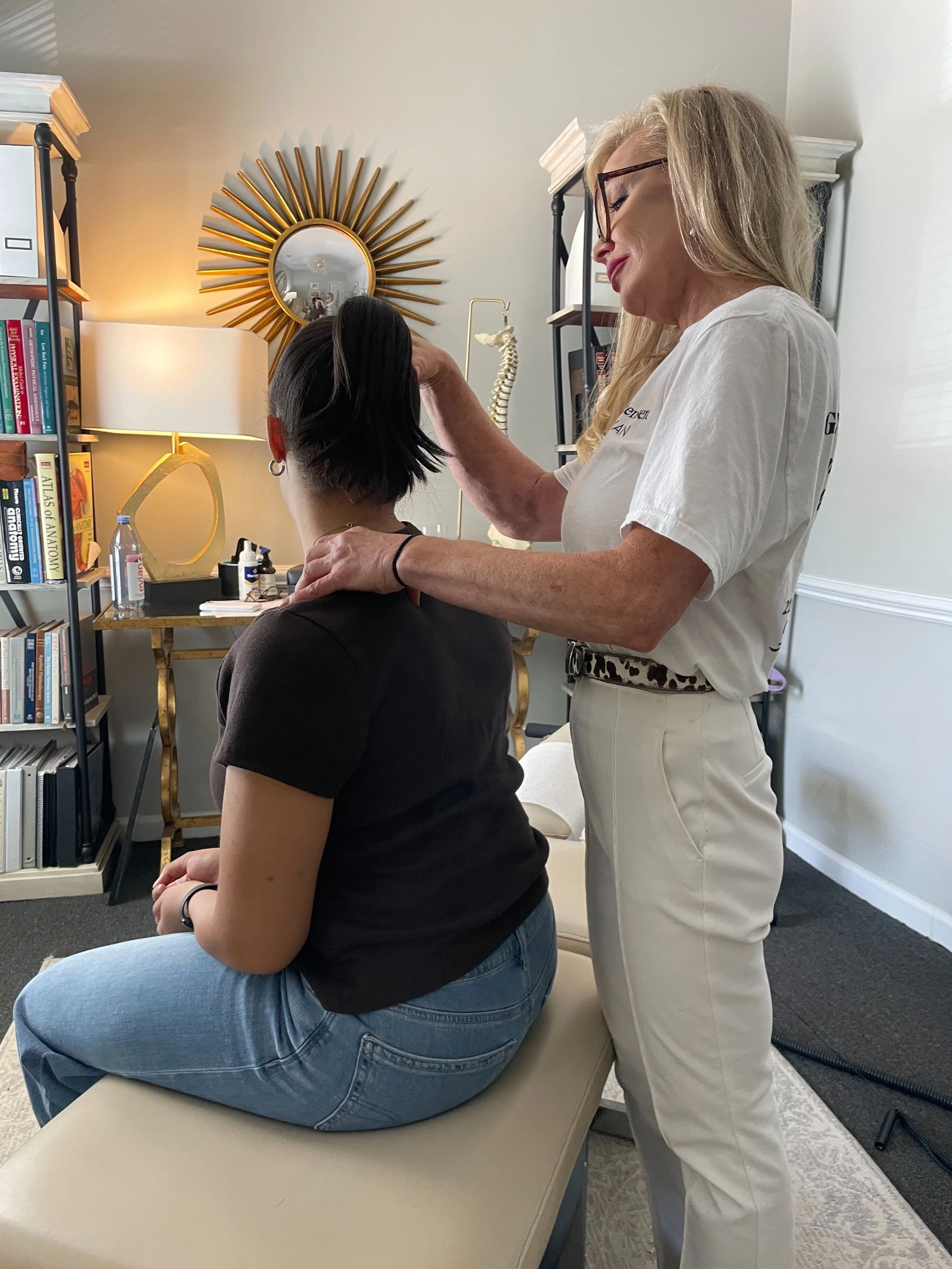 chiropractor dressed in white standing behind patient who is sitting on chiropractic table