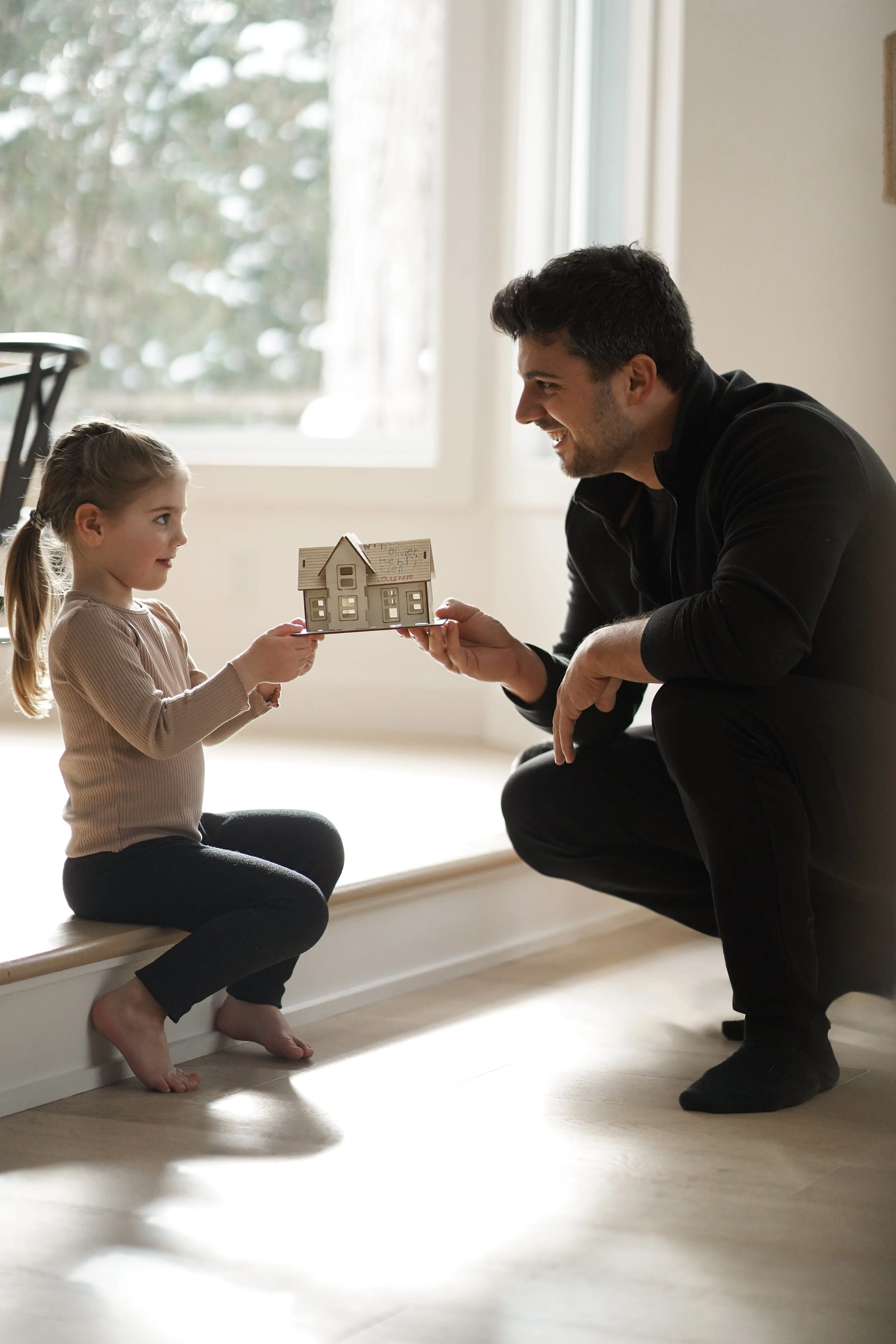 Un homme et une jeune fille s'embrassent en échangeant un petit modèle de maison dans une pièce bien éclairée.