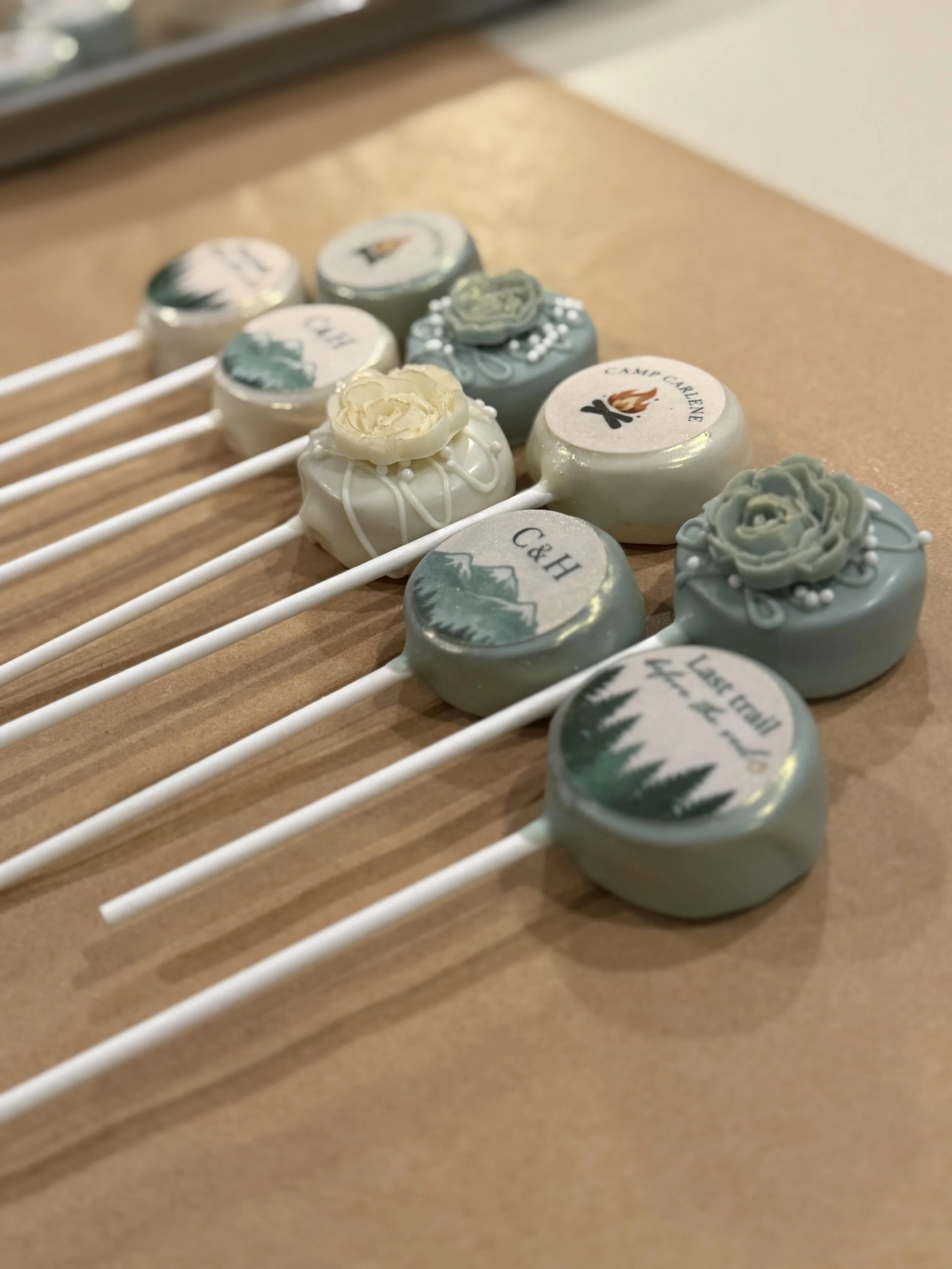 Close-up of decorated lollipops with various logos and designs on sticks, placed on a wooden surface.