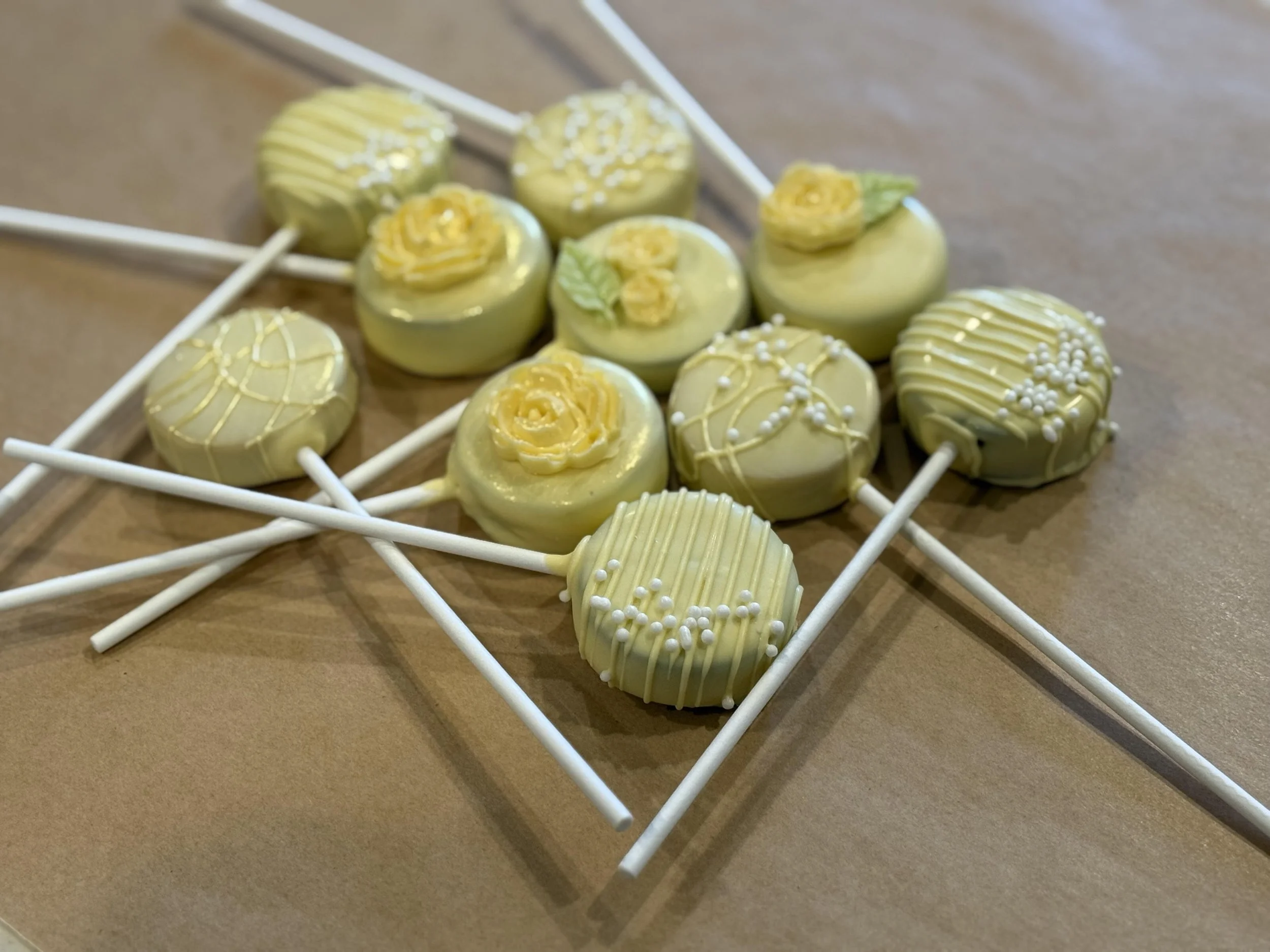 Lemon and green cake pops decorated with white and yellow sprinkles, arranged on a white wire rack.