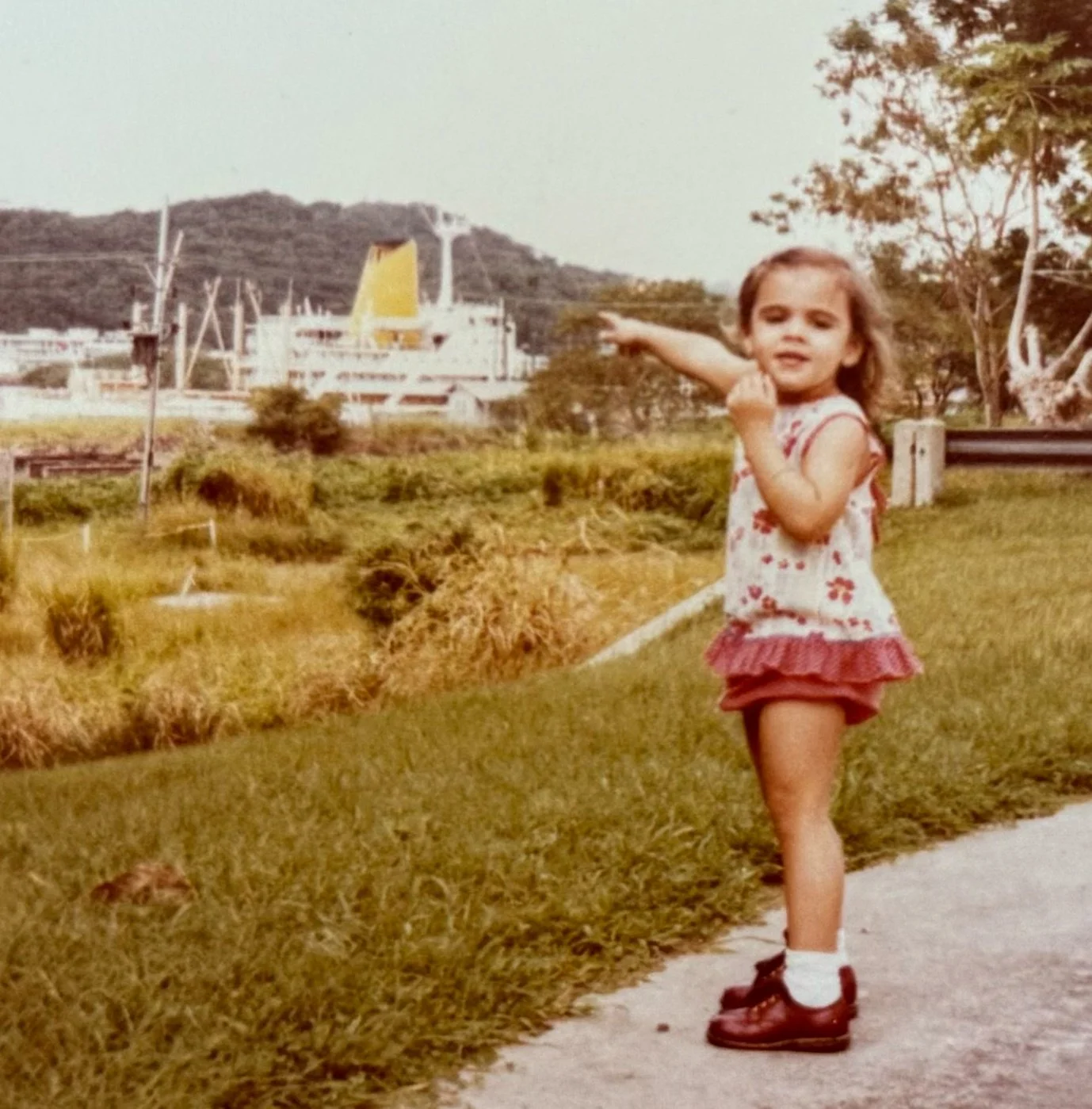 Childhood photo of Devon Holzwarth standing outdoors near a hillside neighborhood in Panama.
