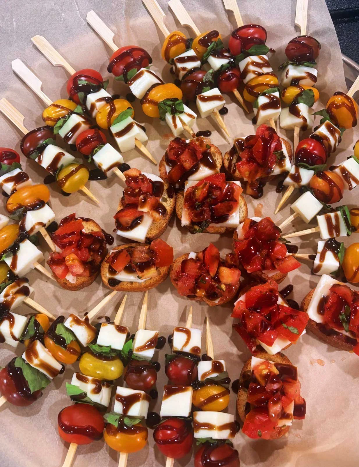 Skewers with cherry tomatoes, mozzarella cheese, basil leaves, and balsamic glaze, served on bread slices with chopped tomatoes on top.